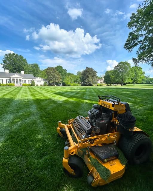 Yellow stand-on mower on a freshly striped estate lawn under a blue sky